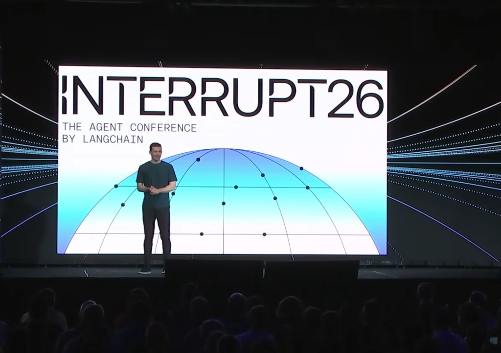 Live photo from Interrupt 2026 at The Midway in San Francisco: Harrison Chase on stage in front of a large INTERRUPT26 backdrop with the audience visible in the foreground.